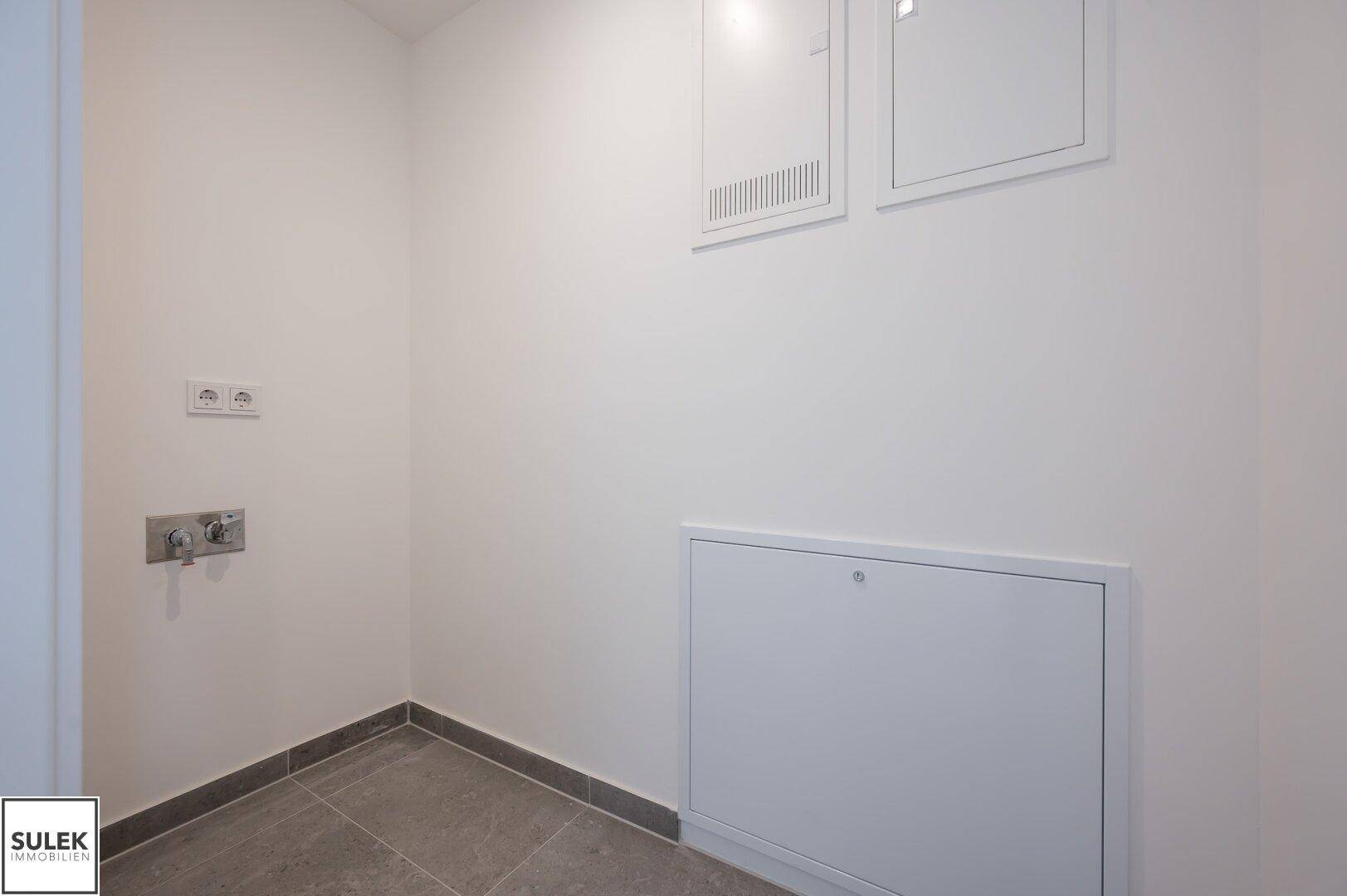 Praktischer Abstellraum mit Anschlüssen für Waschmaschine und Sicherungskästen an der Wand.