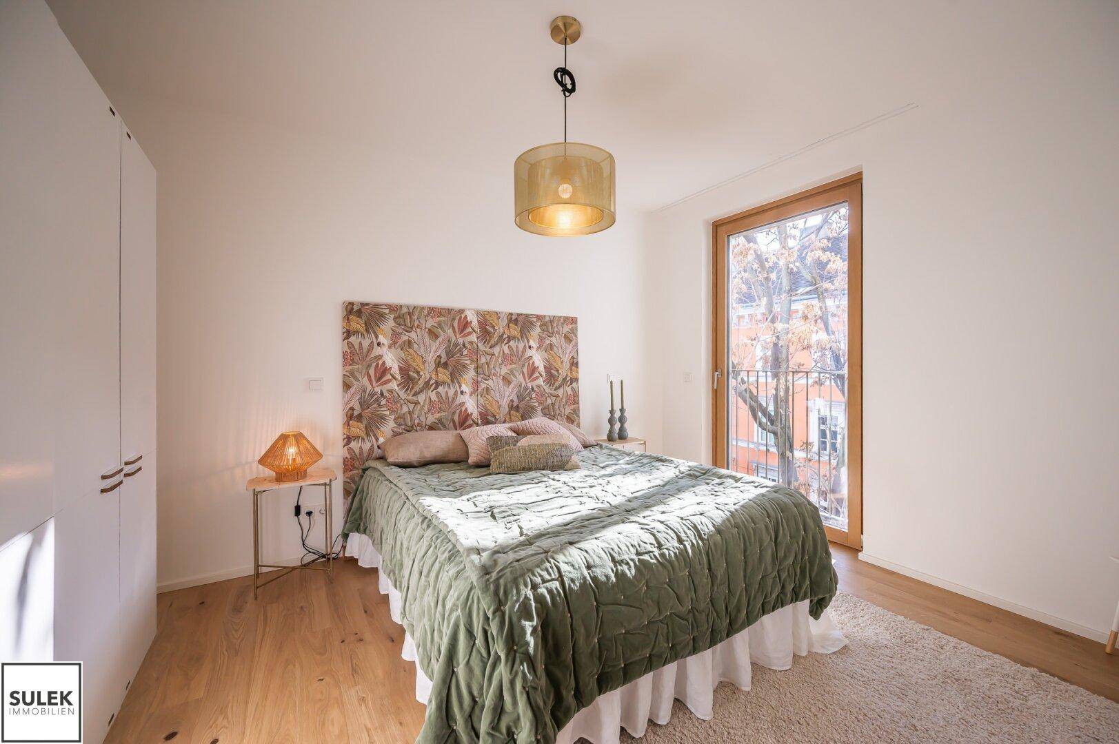 Helles Schlafzimmer mit Holzboden, großem Bett und Zugang zu einem französischen Balkon.