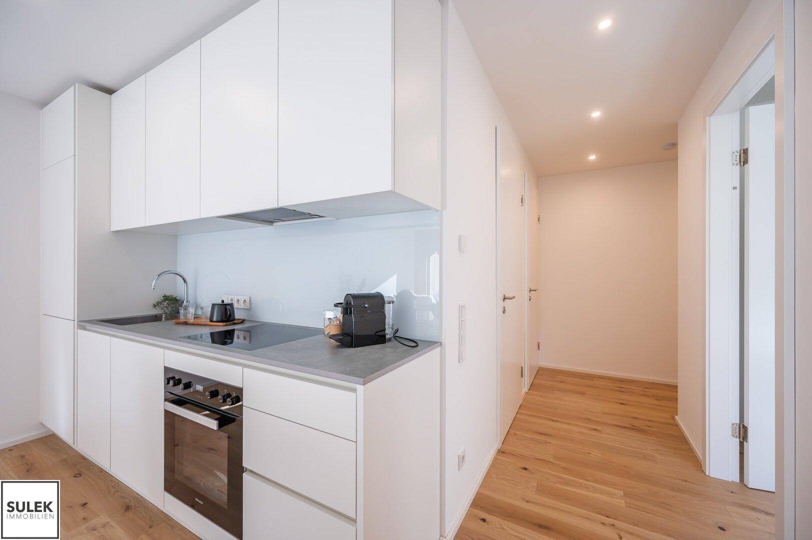 Moderne Einbauküche mit weißen Schränken, Kochfeld und Backofen.