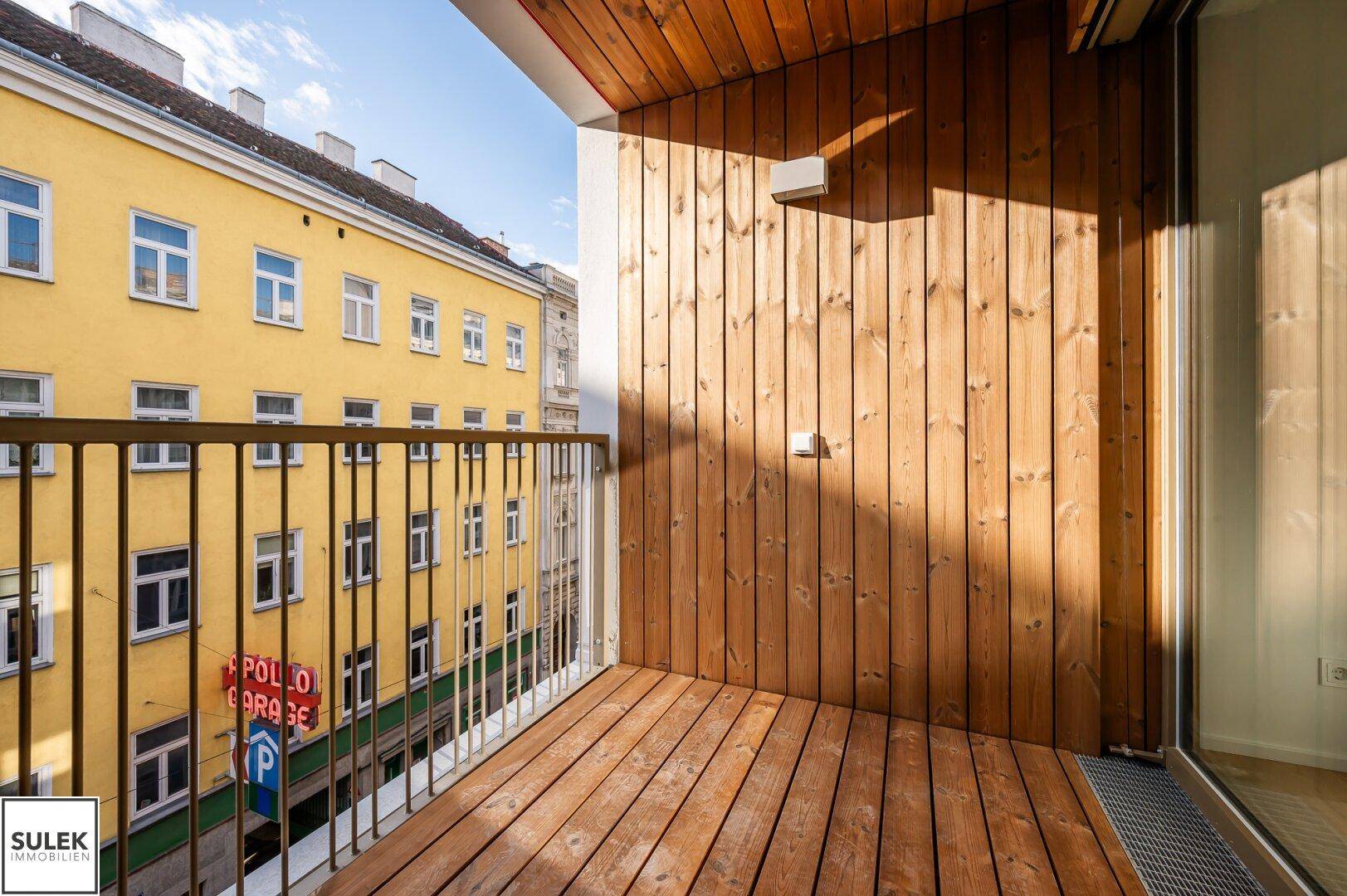 Sonnige Loggia mit Holzboden und Blick auf die umliegende Stadtbebauung.