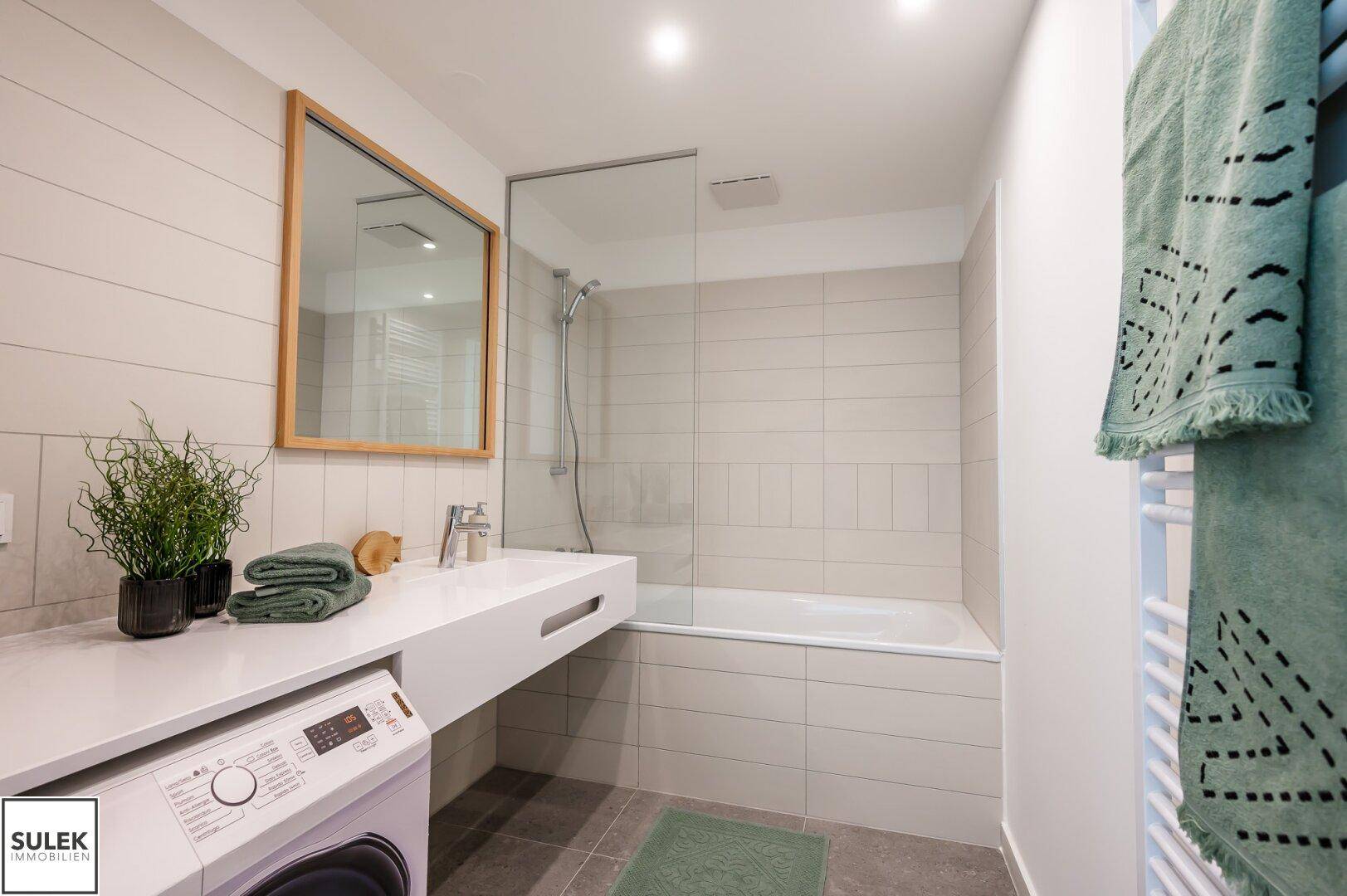 Modernes Badezimmer mit Badewanne, Waschmaschine und beheiztem Handtuchhalter.