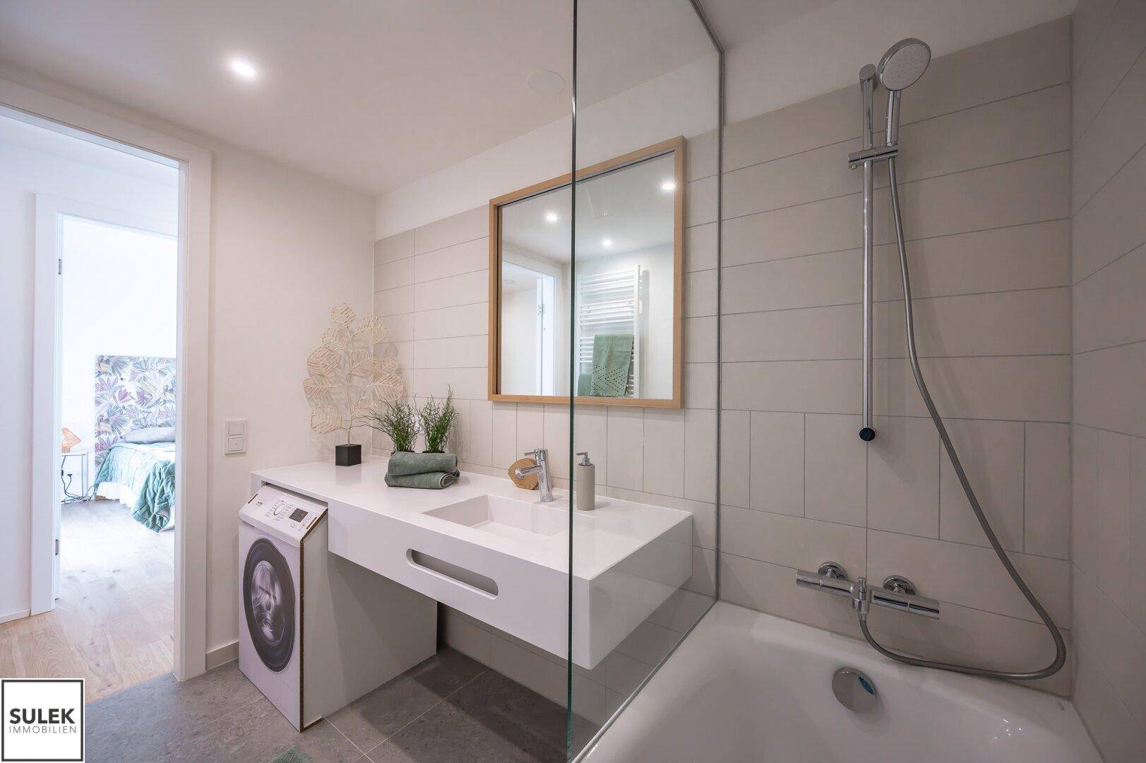 Modernes Badezimmer mit Badewanne, Waschmaschine und großem Spiegel.