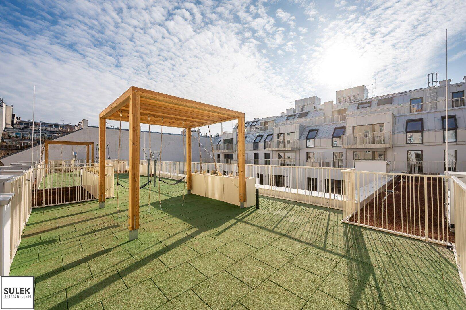 Weitläufiger Dachspielplatz mit grünen Bodenbelägen und Holzpergola.