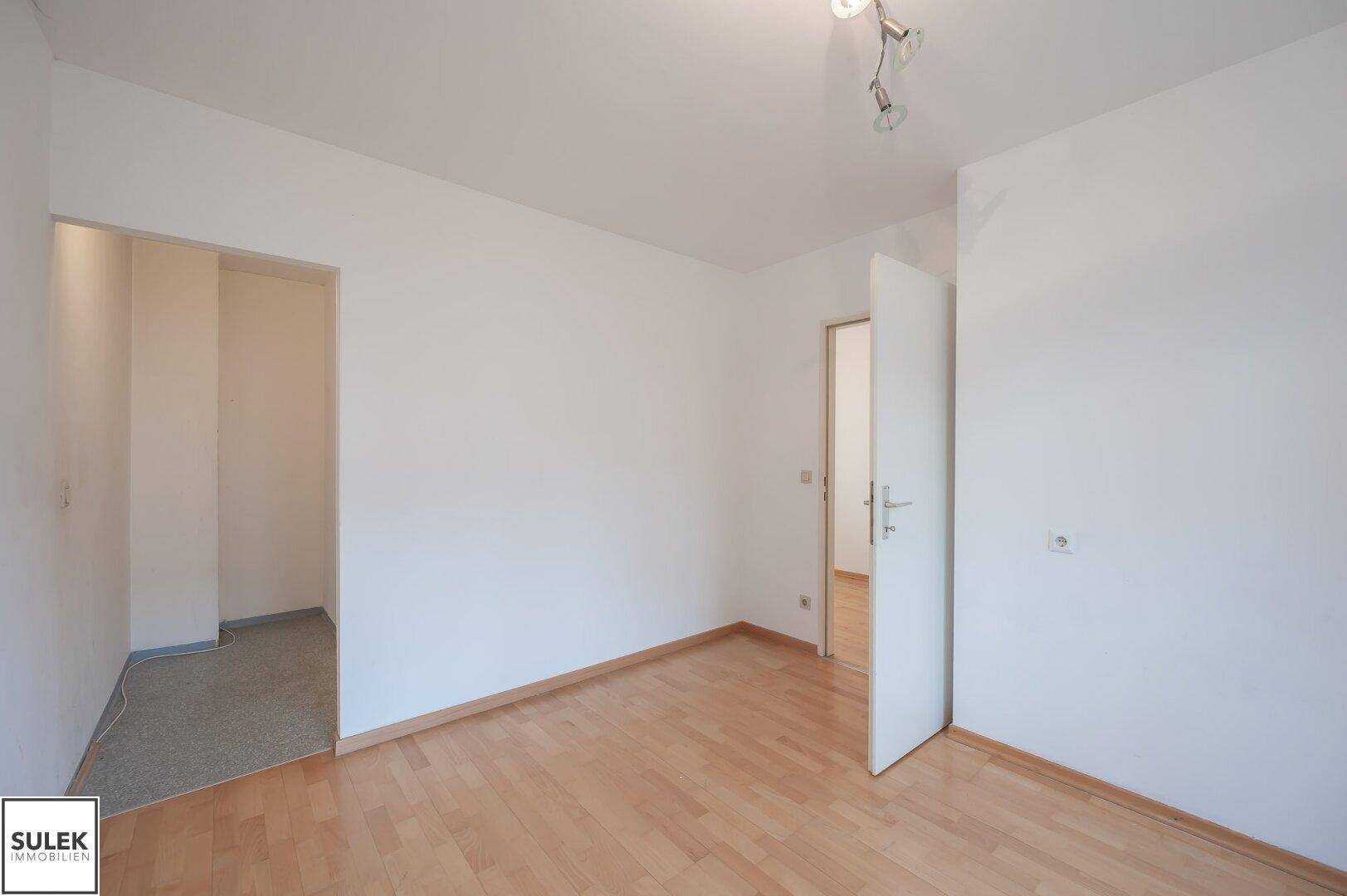 Helles Zimmer mit Parkettboden und Zugang zu einem angrenzenden kleineren Bereich.