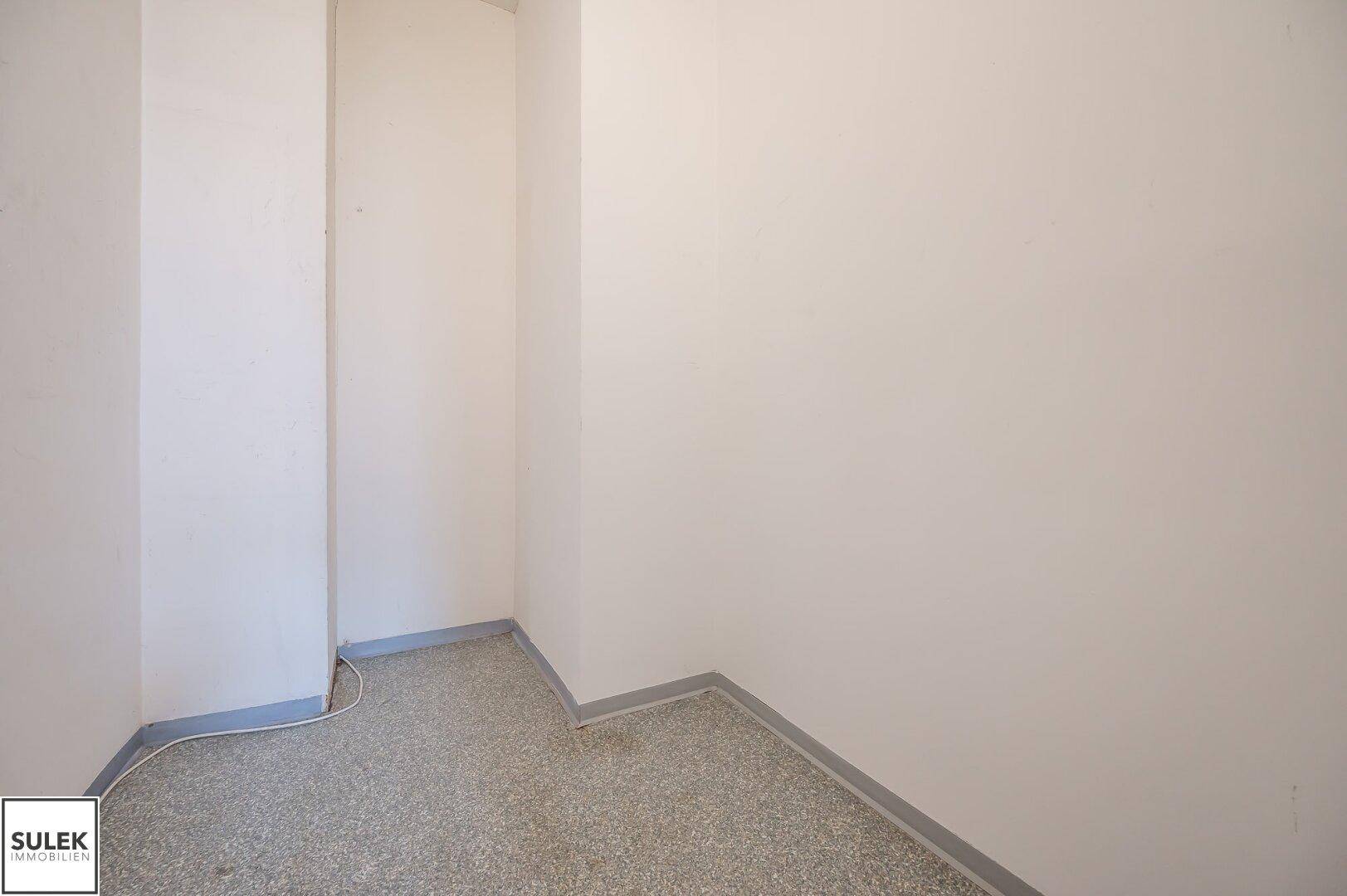 Kleiner, leerer Raum mit grauem Terrazzoboden und weißen Wänden.