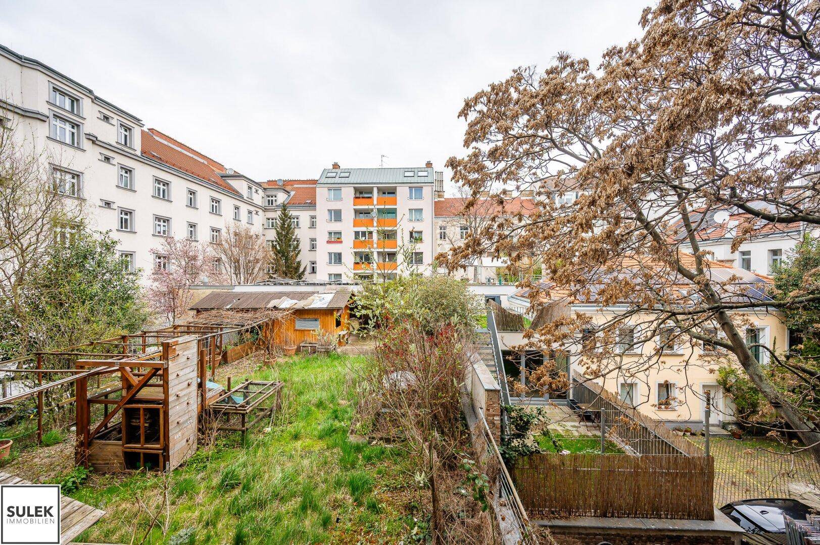 Blick auf einen gemeinschaftlichen Gartenbereich mit Bäumen, Sträuchern und kleinen Gartenhäusern.