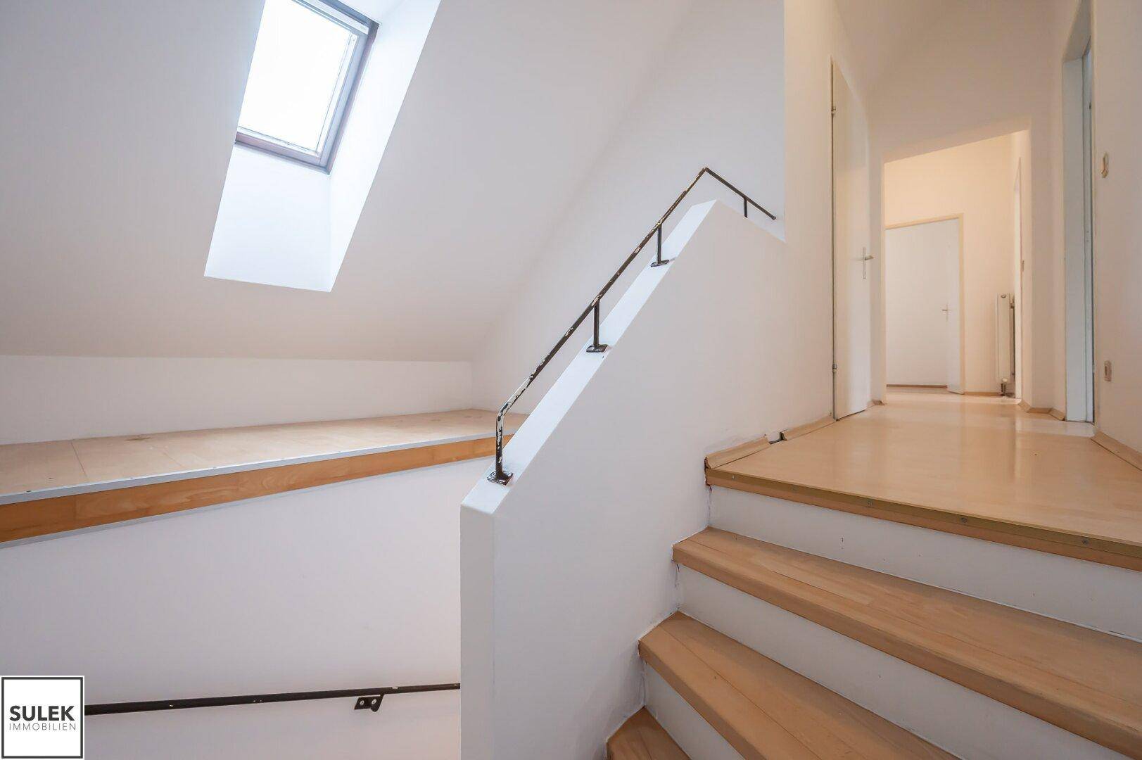 Treppenaufgang im Dachgeschoss mit Holzstufen, schrägen Wänden und einem Dachfenster.