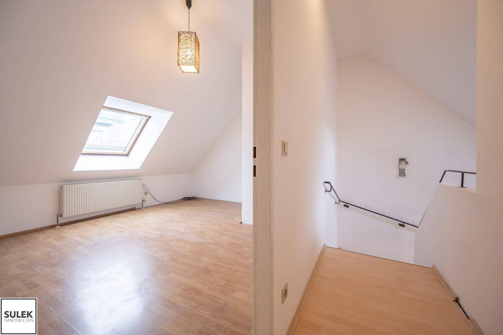 Helles Dachgeschosszimmer mit Parkettboden, schrägen Wänden und einem großen Dachfenster.