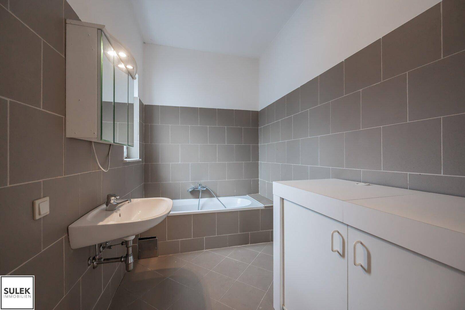 Modern gefliestes Badezimmer mit Badewanne, Waschbecken und Spiegelschrank.