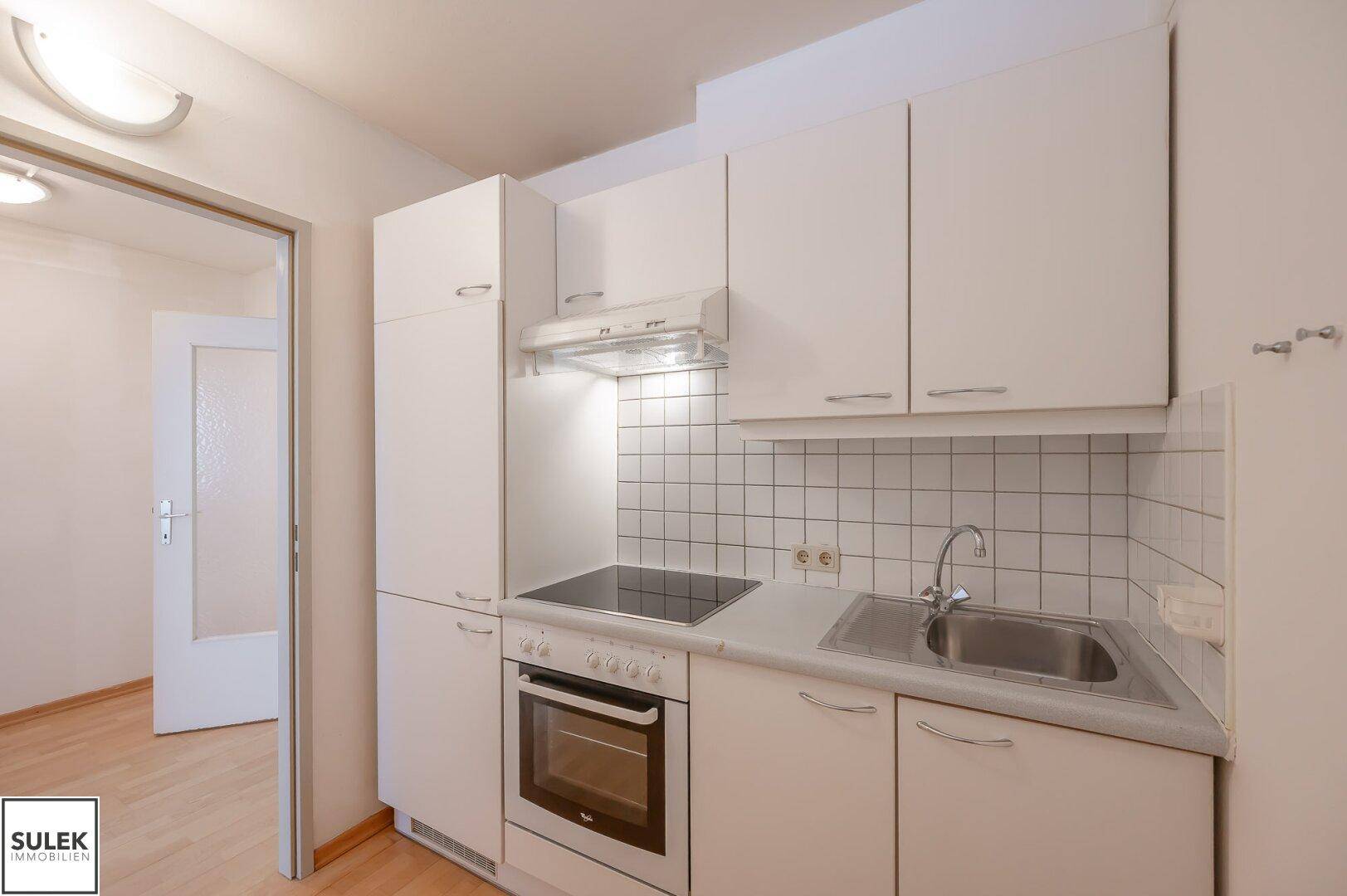 Kompakte Einbauküche mit weißen Schränken, Kochfeld, Backofen und Spüle.