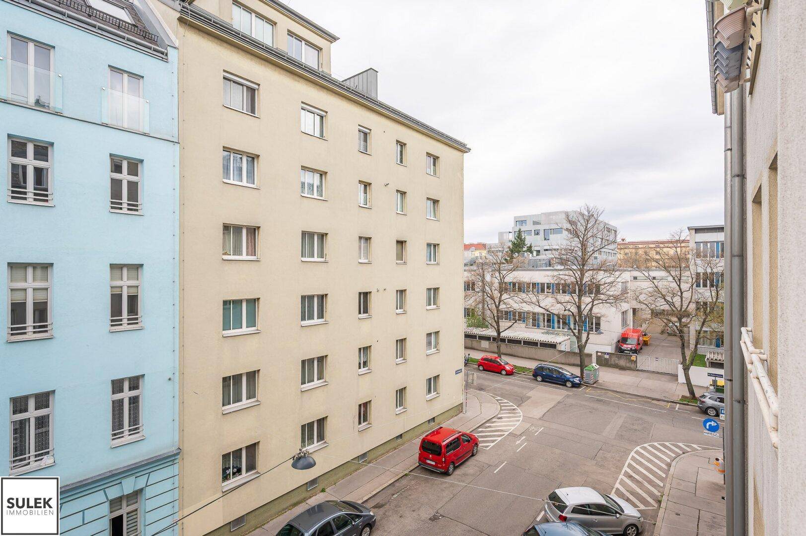 Blick auf eine städtische Straße mit geparkten Autos und angrenzenden Wohngebäuden.