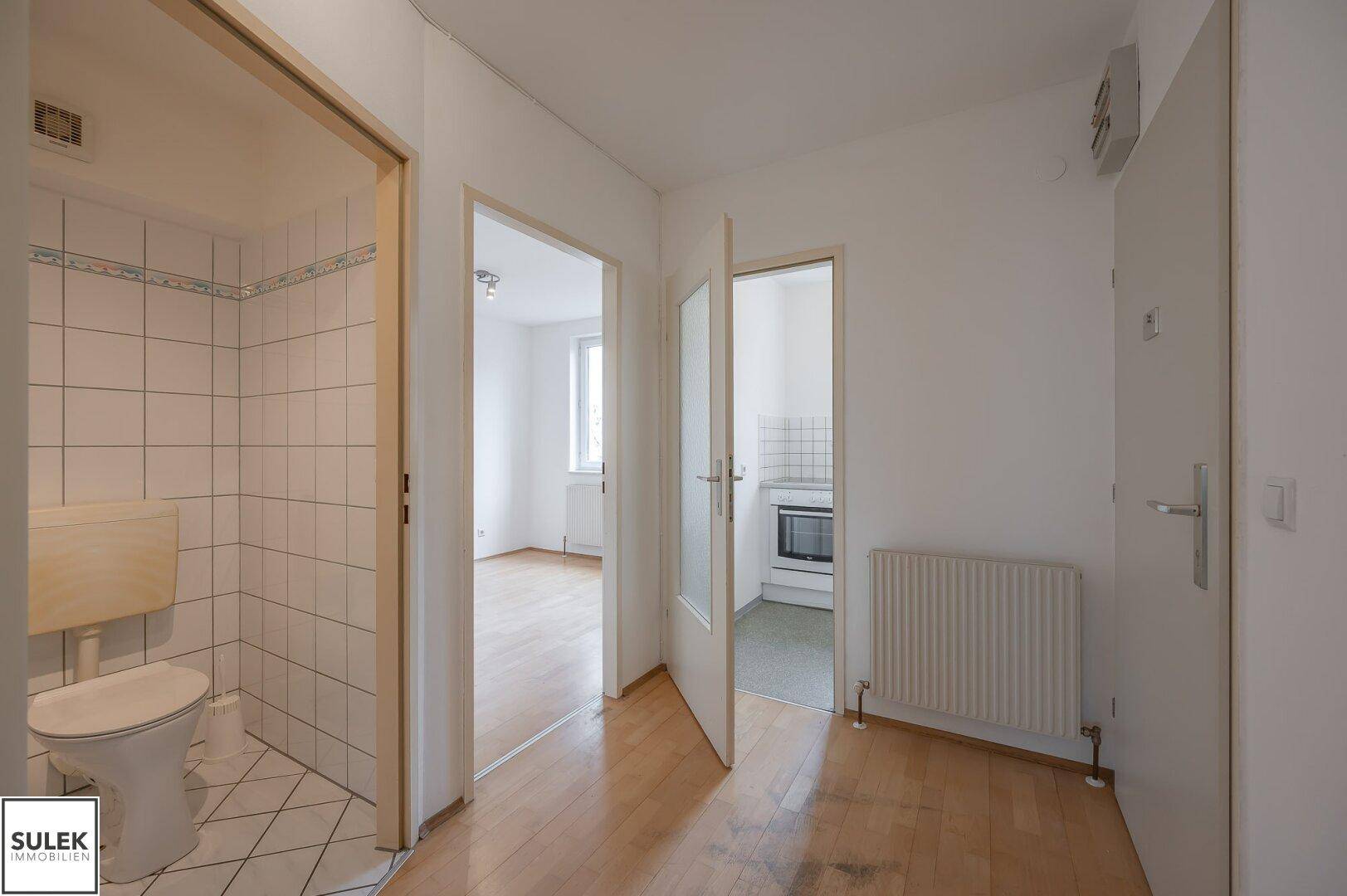 Flur mit Parkettboden und Zugang zu einer separaten Toilette und einer Küche.