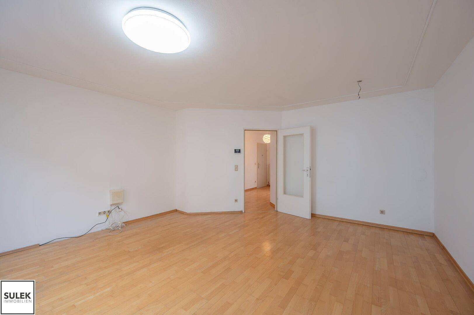 Geräumiges Wohnzimmer mit Parkettboden und heller Deckenleuchte.