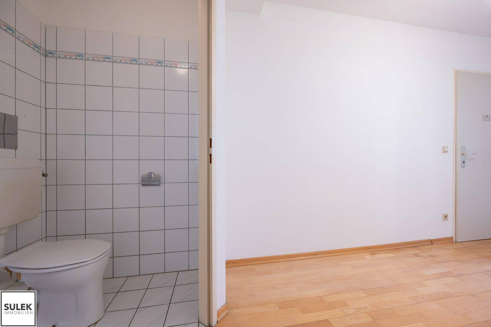 Separate Toilette mit weißen Fliesen und einfacher Ausstattung.