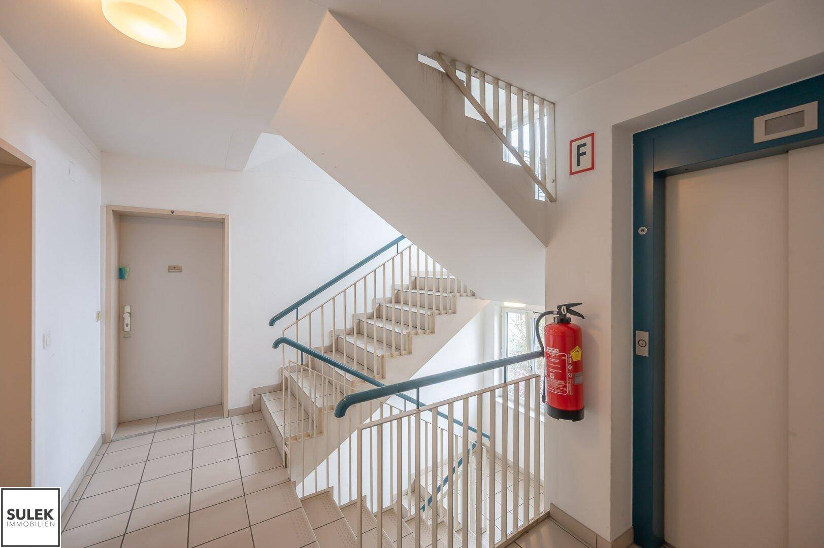 Geräumiges Treppenhaus mit Aufzug und breiter Treppe.