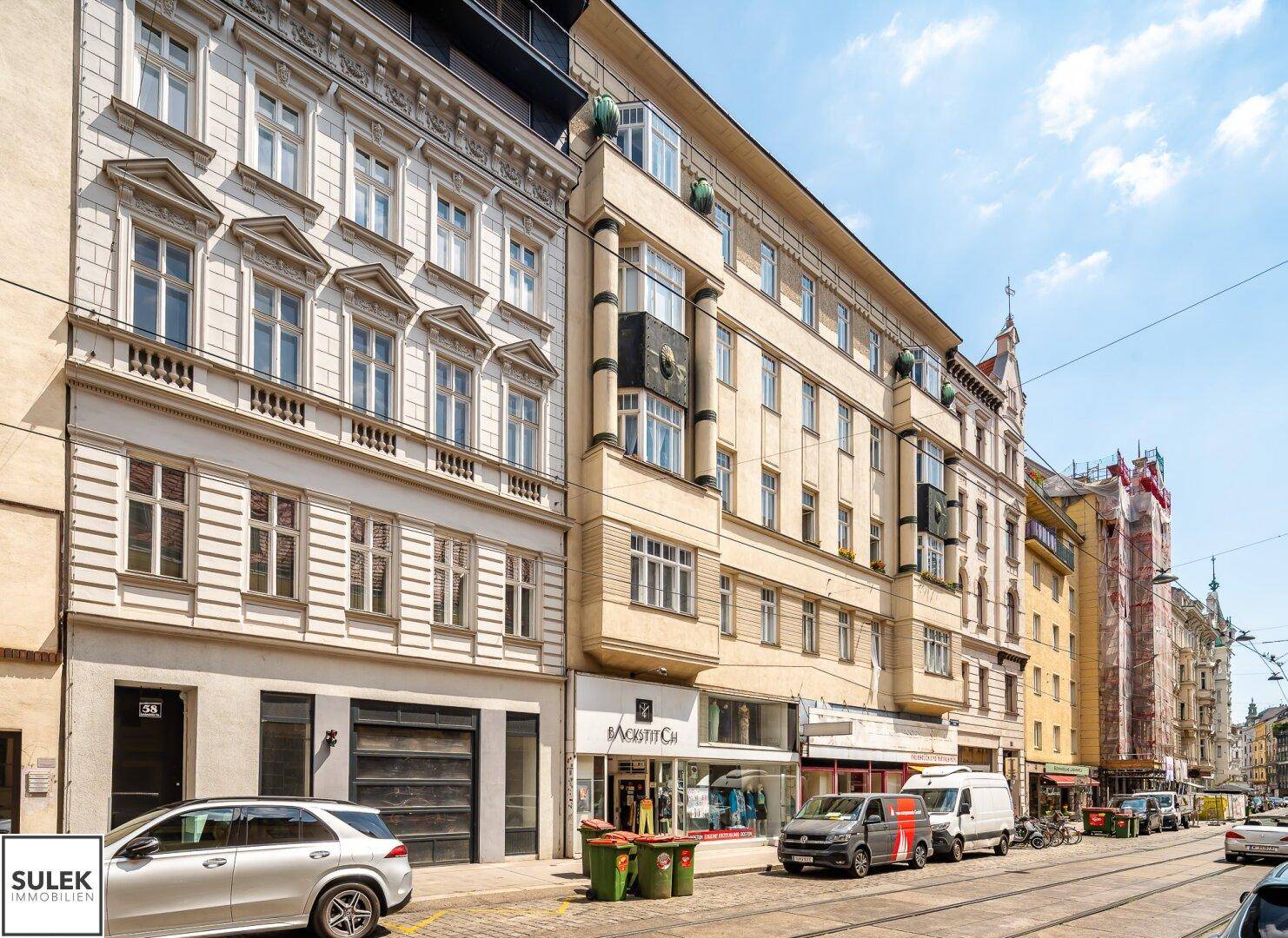 Historische Straßenansicht mit Gebäudefassaden, Geschäften und parkenden Autos.