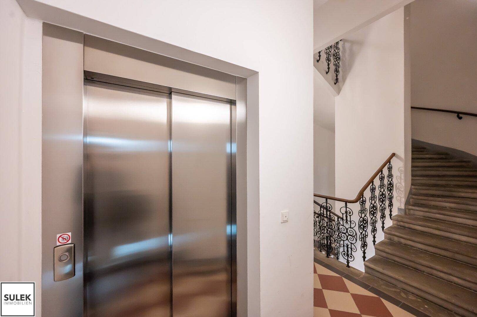 Moderner Aufzug im Treppenhaus mit klassischem Geländer und Fliesenboden, für bequemen Zugang.