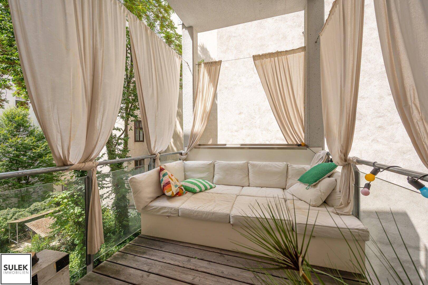Einladender Balkon mit bequemer Lounge-Sitzgruppe und Vorhängen für Privatsphäre, umgeben von Grün.