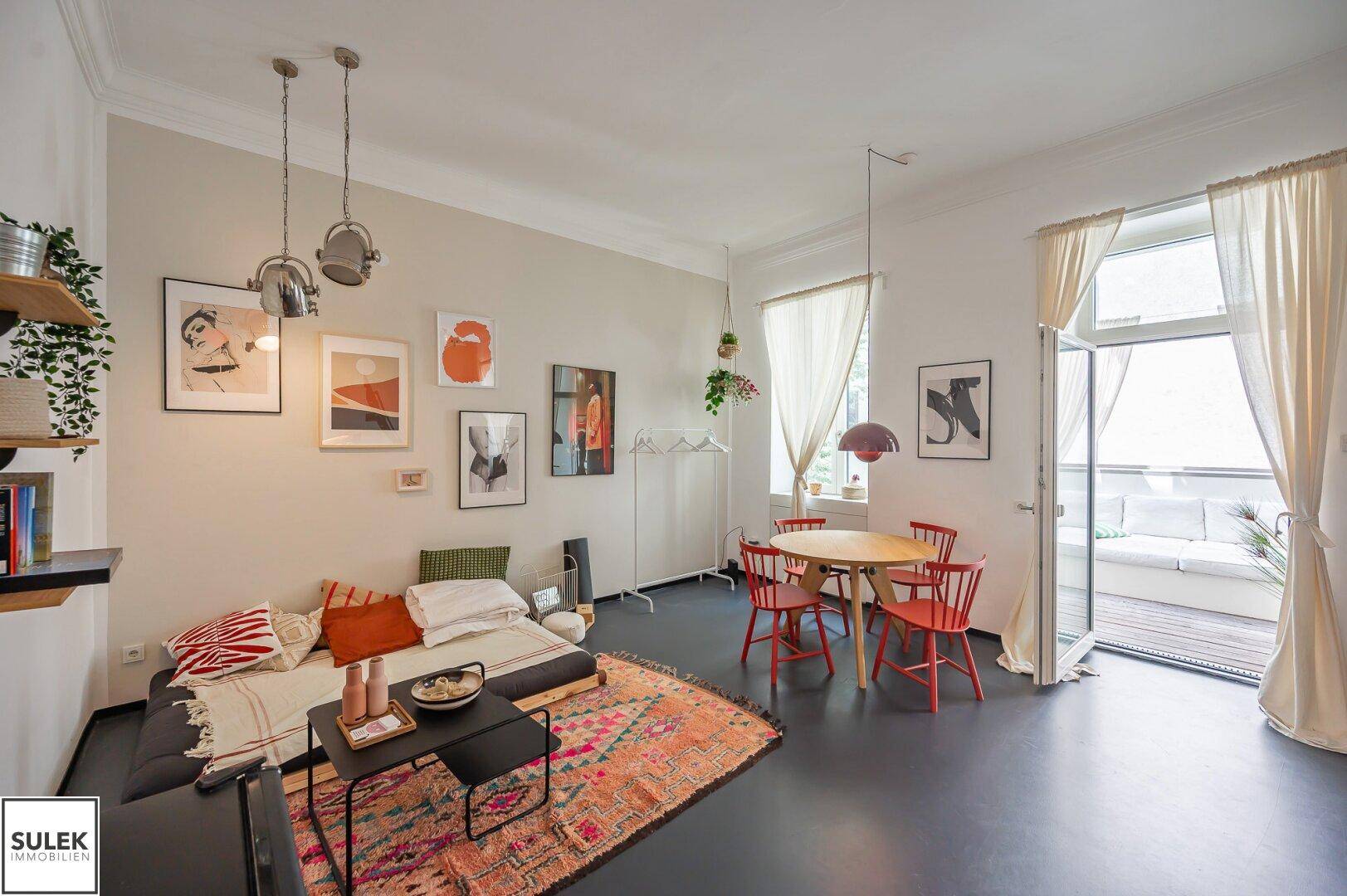 Gemütlicher Wohn-Essbereich mit farbenfrohem Teppich, Sofa und Zugang zum Balkon, hell durch große Fenster.
