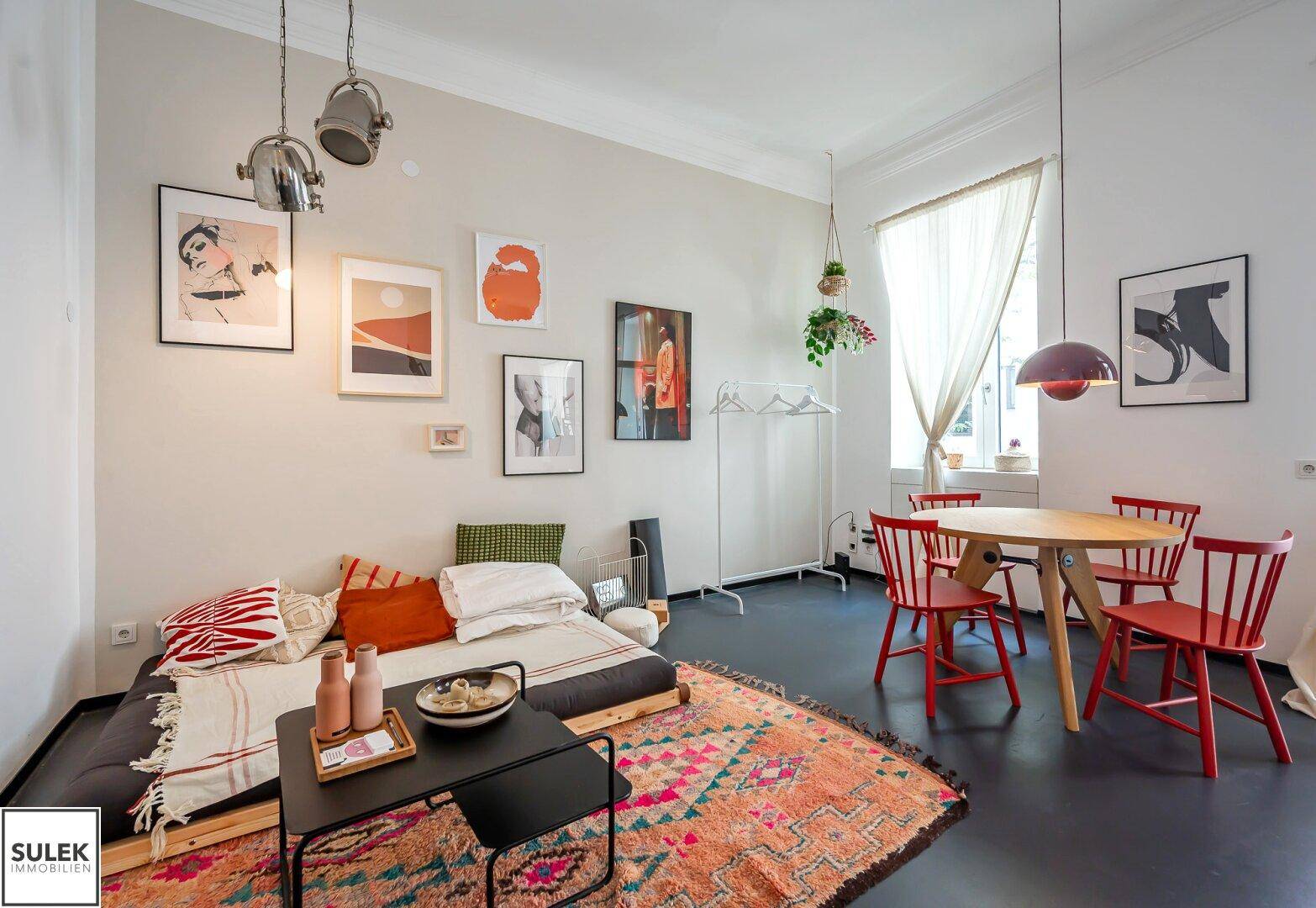 Geräumiger Wohn-Essbereich mit Sofa, Esstisch und farbenfrohem Teppich, hell durch große Fenster.