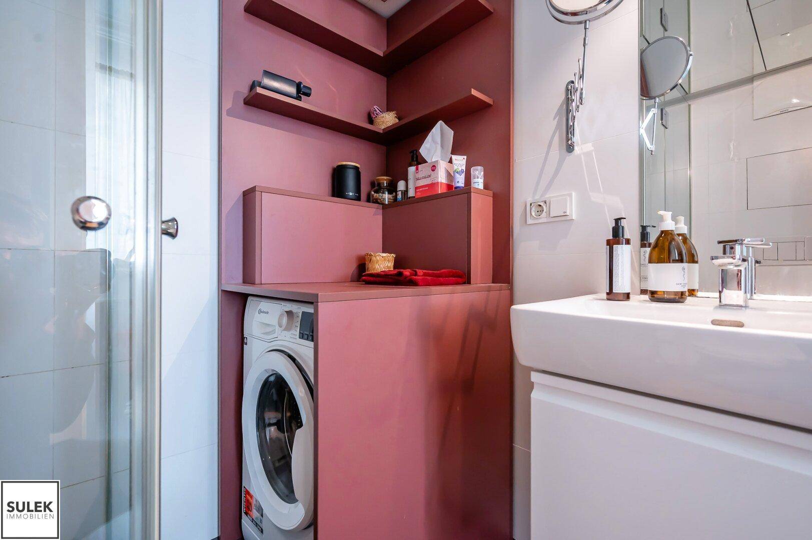 Funktionales Badezimmer mit Waschmaschine, Waschtisch und Ablagen in einem modernen Design.
