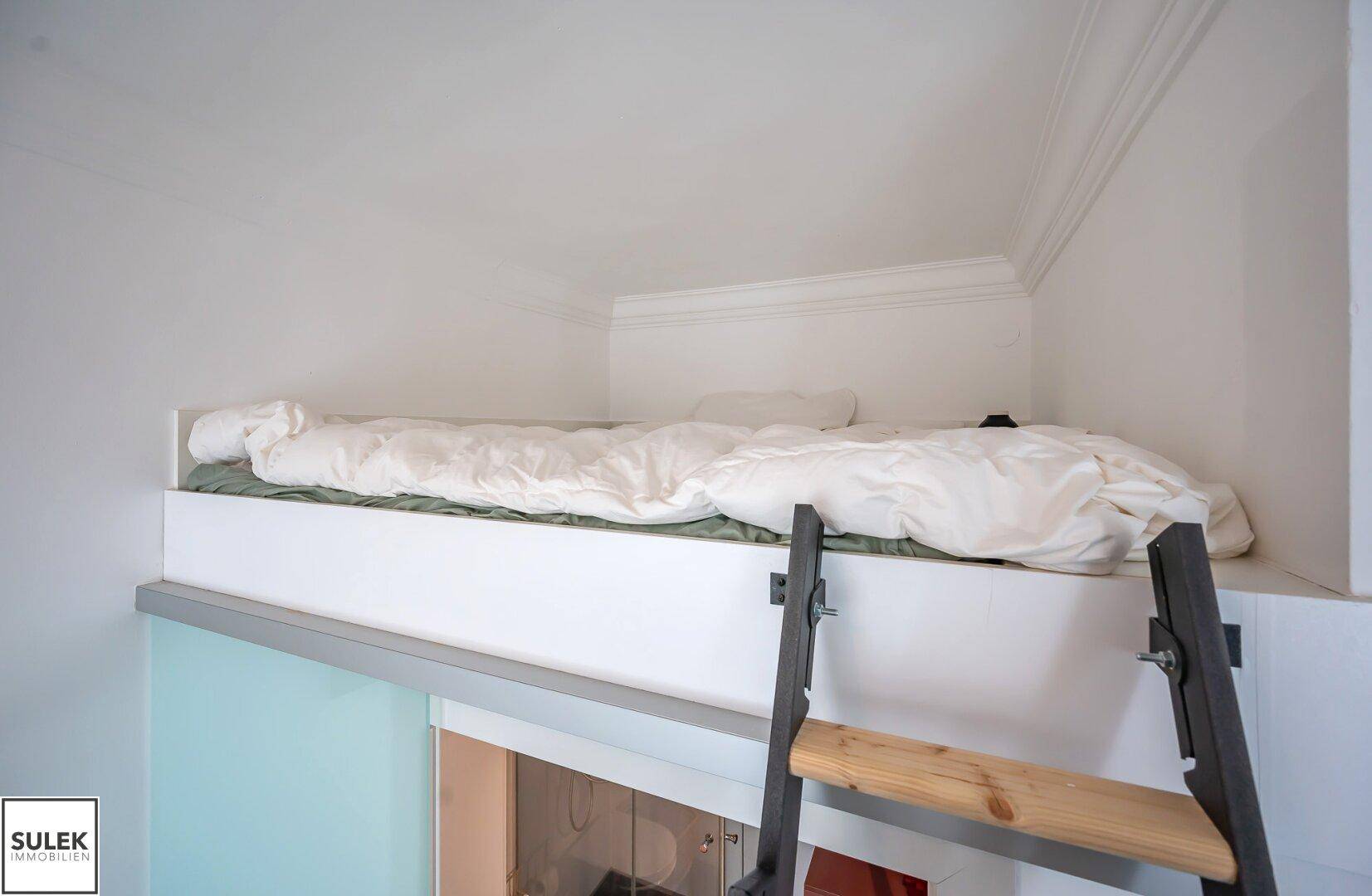 Gemütliches Hochbett mit weißer Bettwäsche, zugänglich über eine Leiter, bietet einen separaten Schlafbereich.