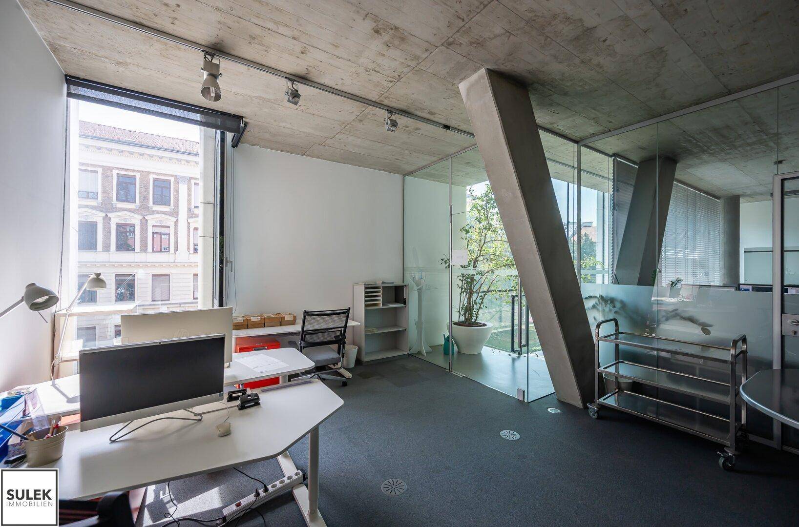 Arbeitsplatz in einem modernen Büro mit Sichtbetondecke, großem Fenster und viel Tageslicht.