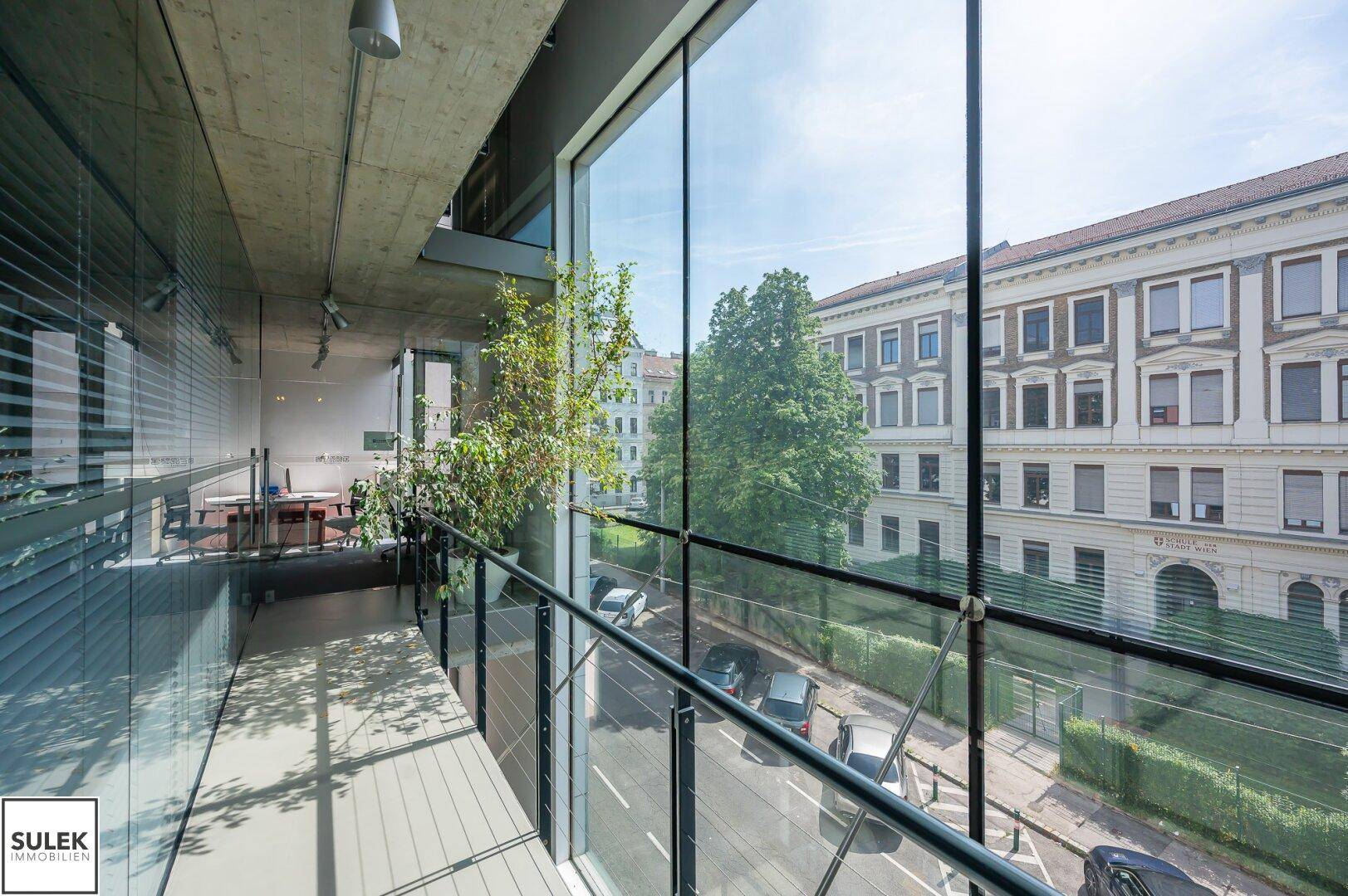 Heller Bürobereich mit raumhohen Fenstern, Blick auf die Straße und Sichtbetondecke.