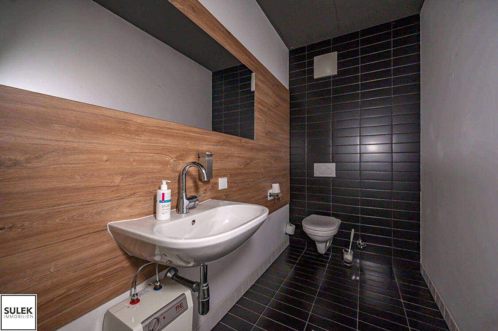 Modernes Gäste-WC mit schwarzen Fliesen, Holzverkleidung und wandmontierter Toilette.