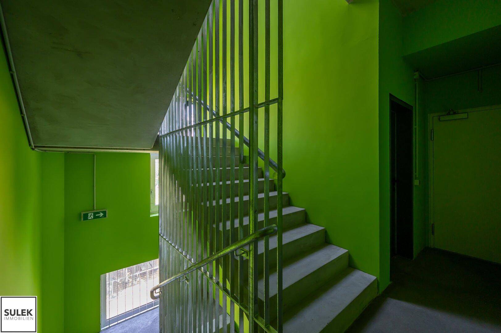 Treppenhaus mit leuchtend grünen Wänden und Metallgeländer, das eine dynamische und moderne Atmosphäre schafft.