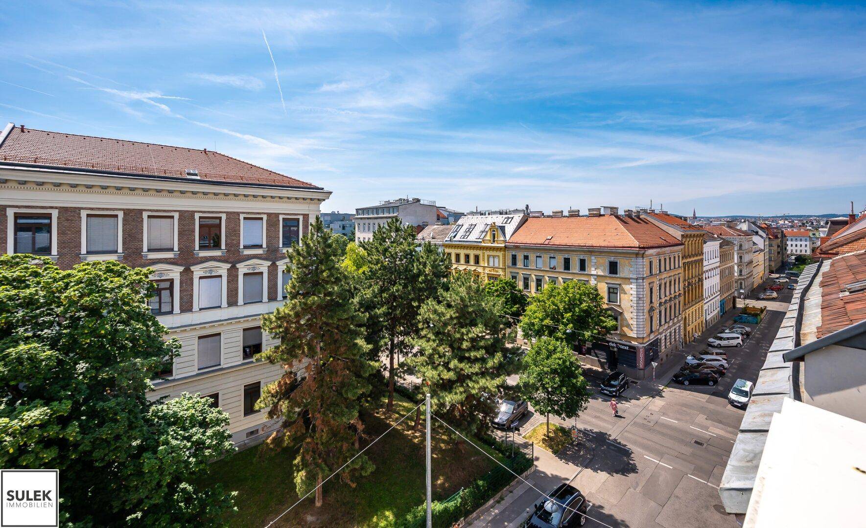Panoramablick von oben auf die Stadt mit Gebäuden, Straßen und viel Grün unter blauem Himmel.