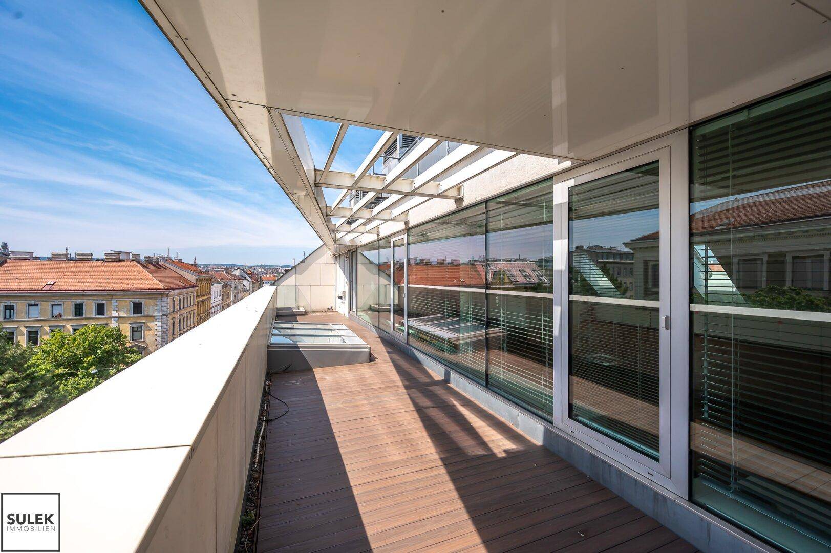 Moderne Terrasse mit Holzboden, Überdachung und großen Glasfronten, die viel Licht hereinlassen.