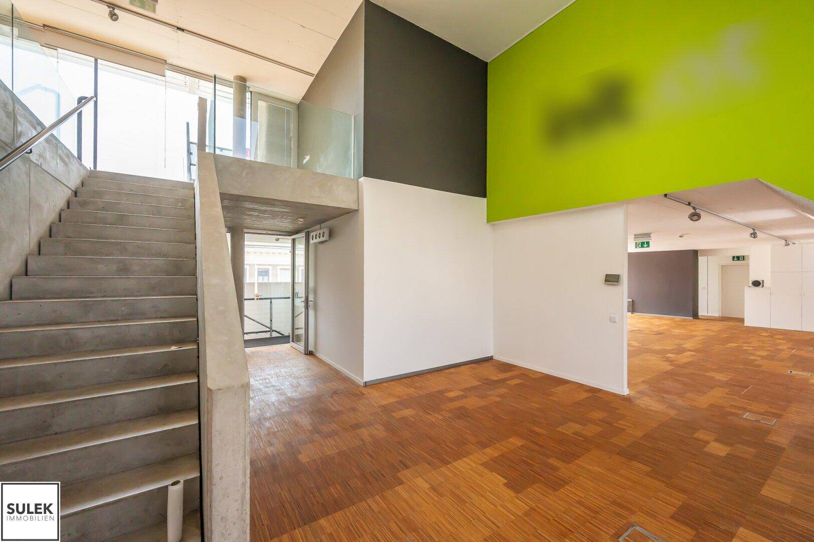 Geräumiger Eingangsbereich mit Treppe, Holzparkettboden und einer leuchtend grünen Akzentwand.