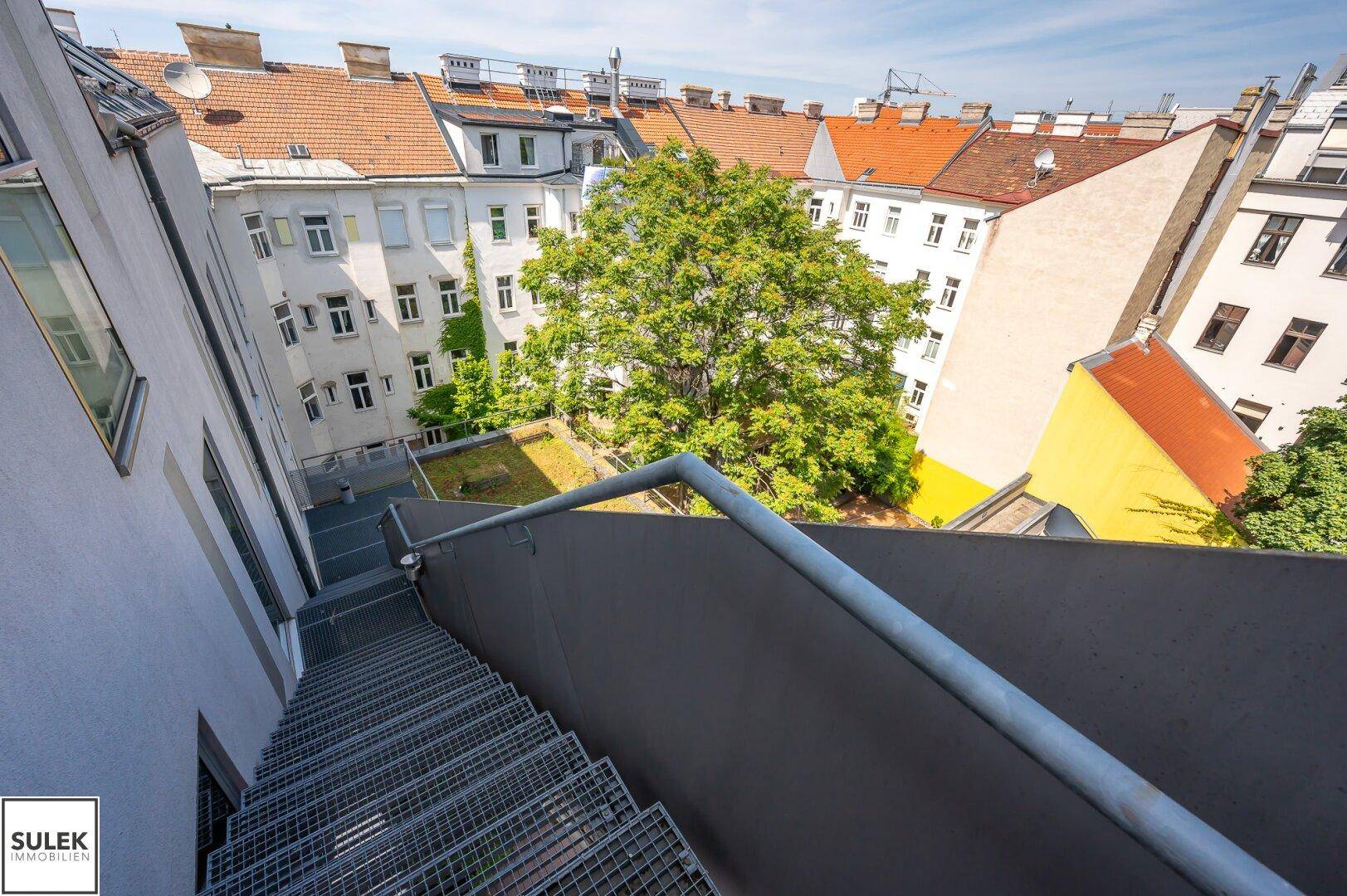 Außentreppe aus Metall führt zu einem begrünten Innenhof zwischen den Gebäuden.