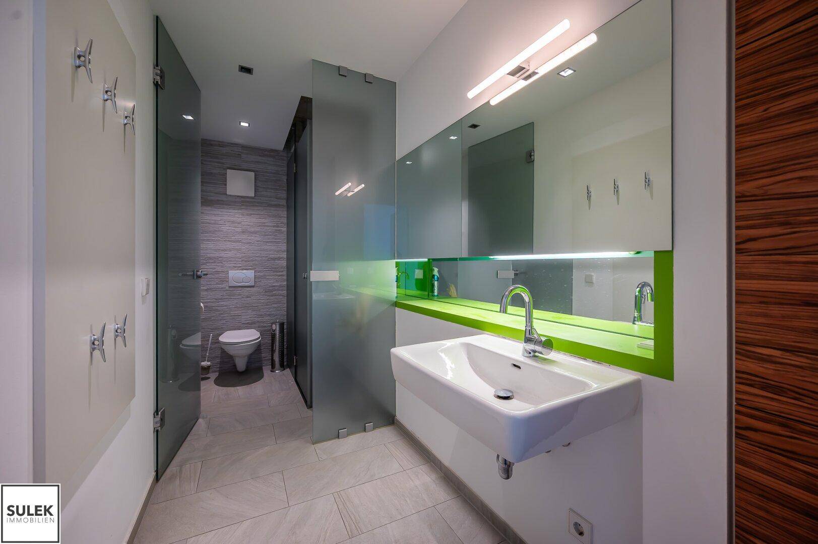 Modernes Badezimmer mit Doppelwaschbecken, Glasabtrennungen und leuchtend grünen Akzenten.