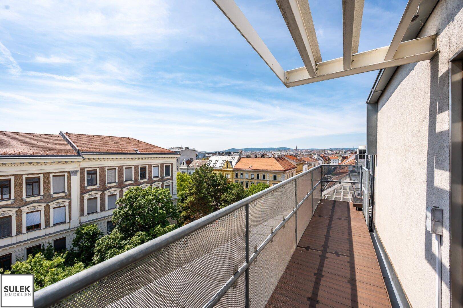 Langer Balkon mit Holzboden und Metallgeländer, bietet einen weiten Blick über die Stadt.