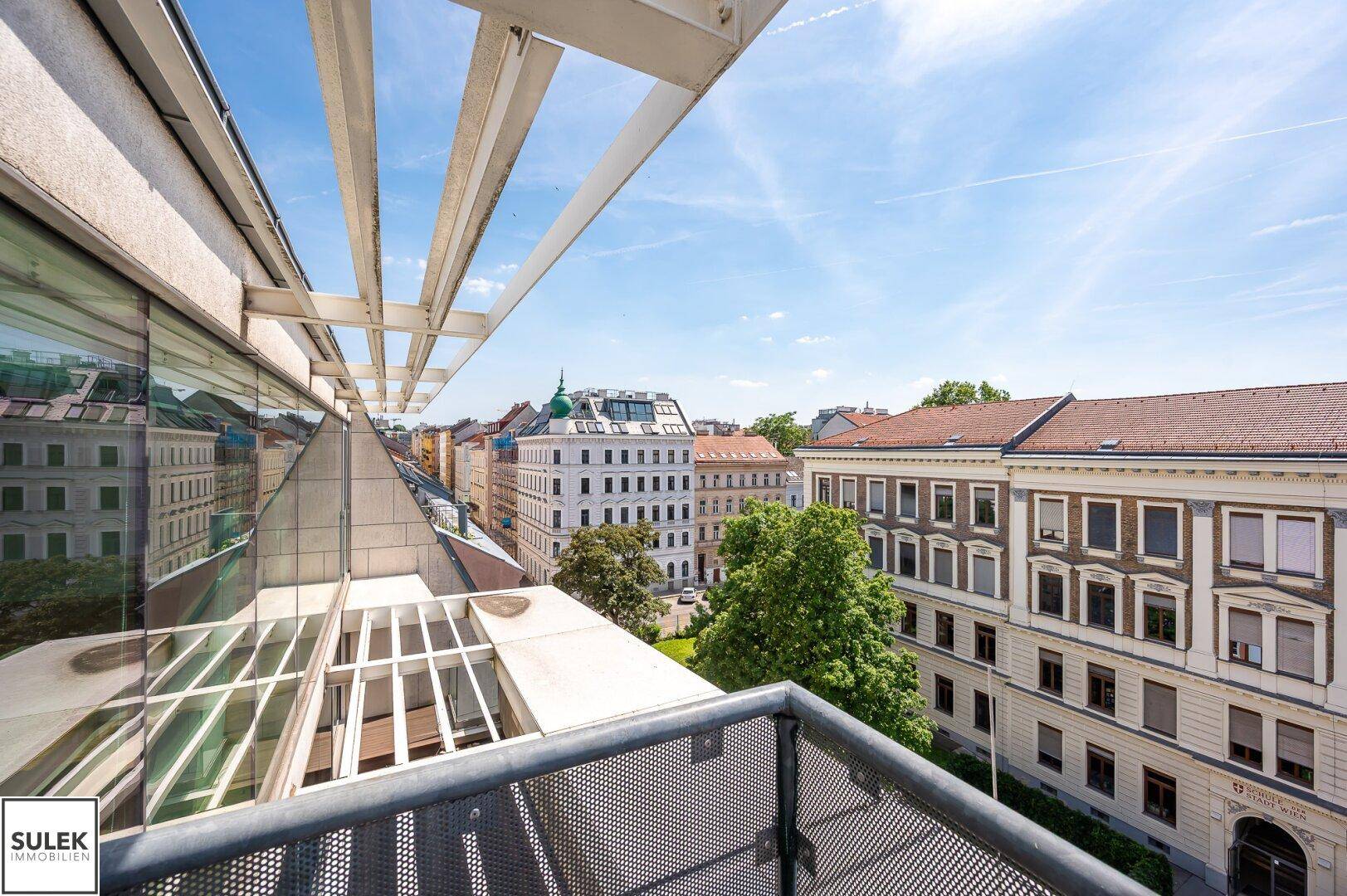 Balkon mit Stadtblick und umliegenden Gebäuden unter blauem Himmel, bietet eine weite Aussicht.