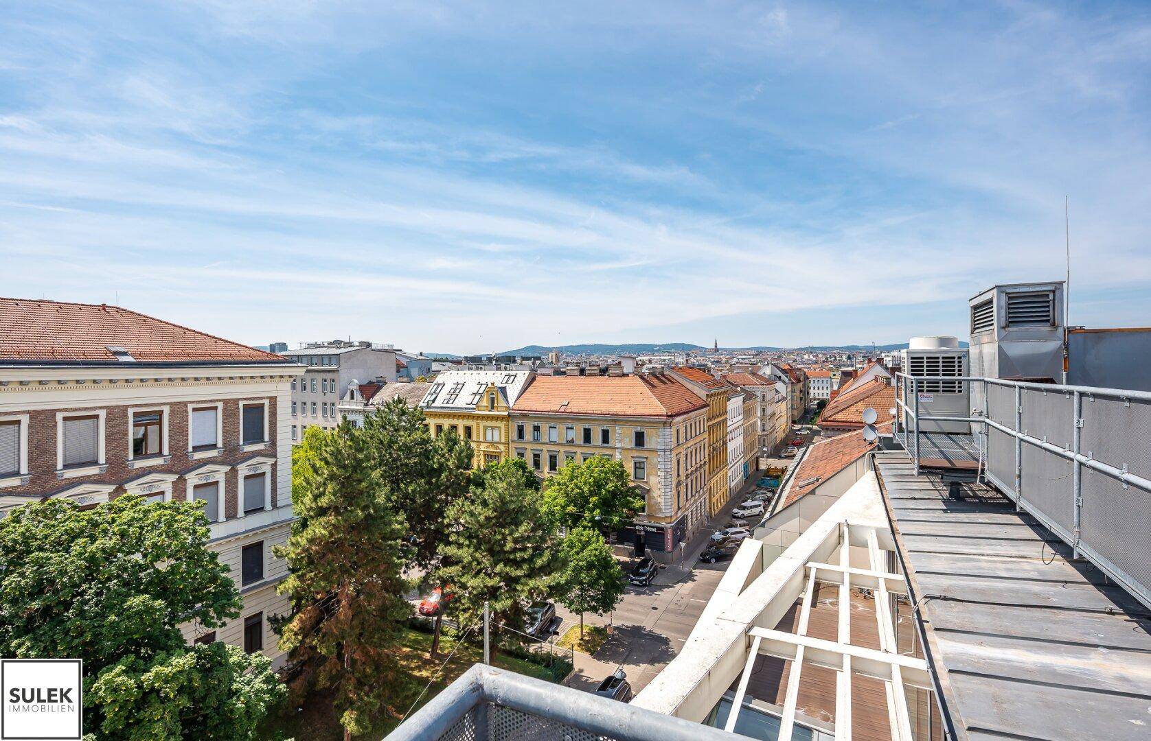 Balkon mit Panoramablick über die Dächer der Stadt und die umliegende Architektur, sonniger Tag.