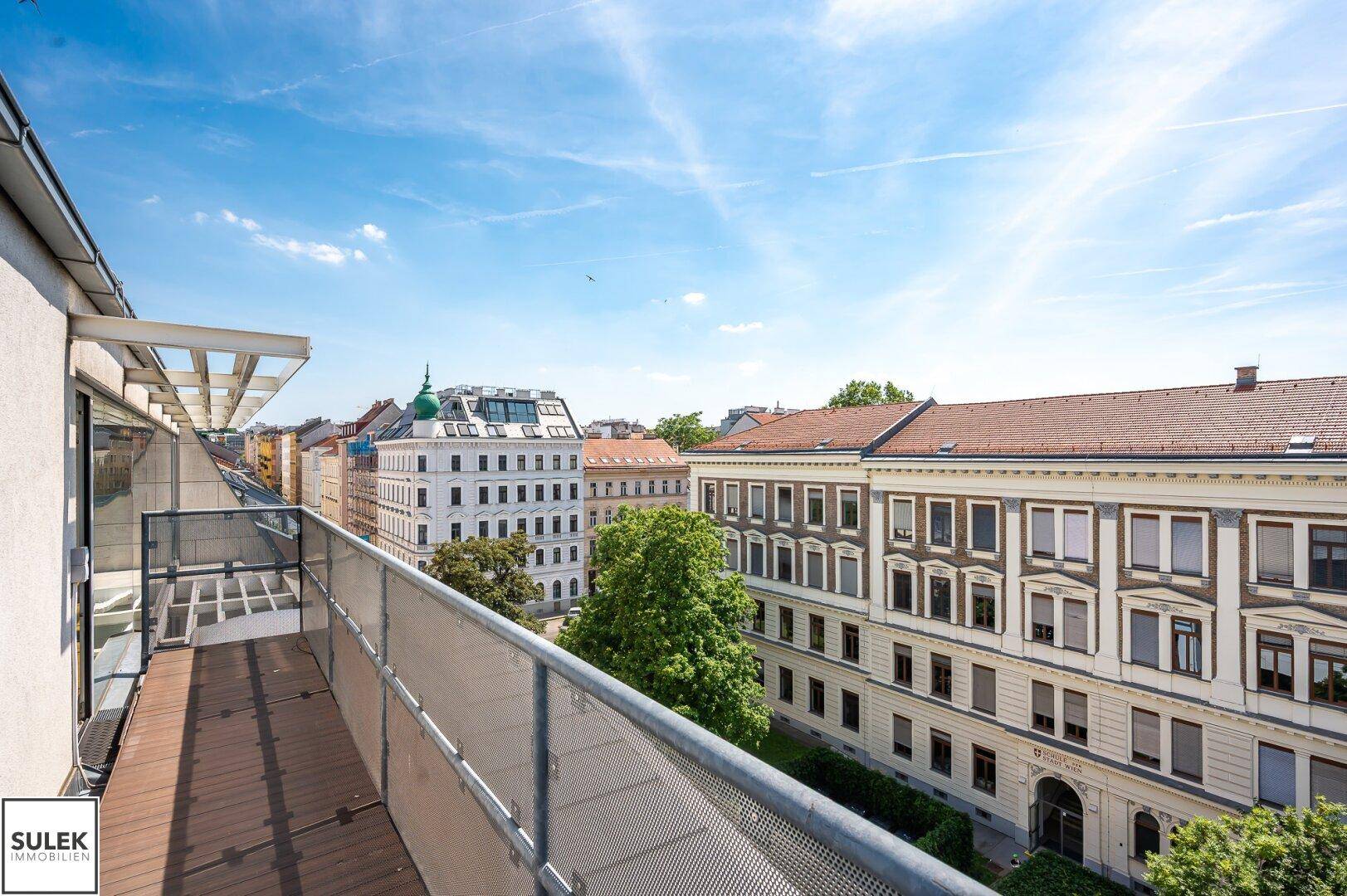 Geräumiger Balkon mit Holzboden und Metallgeländer, bietet einen weiten Blick über die Stadtlandschaft.