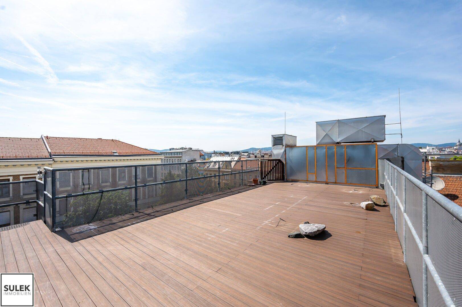 Große Dachterrasse mit Holzboden und weitem Blick über die Dächer der Stadt.