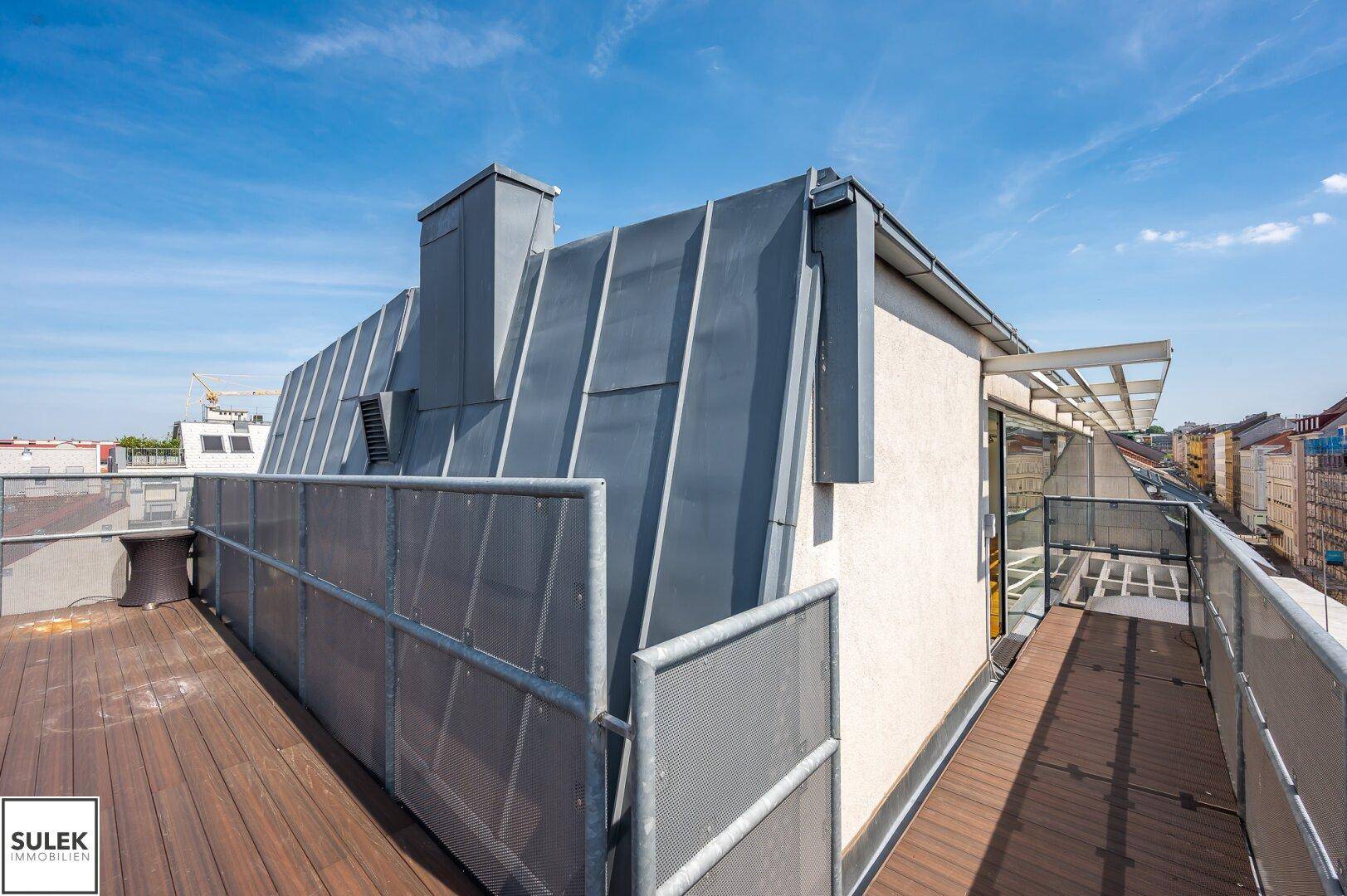 Dachterrasse mit Holzboden und moderner Metallverkleidung, bietet einen Blick auf die Gebäudestruktur.