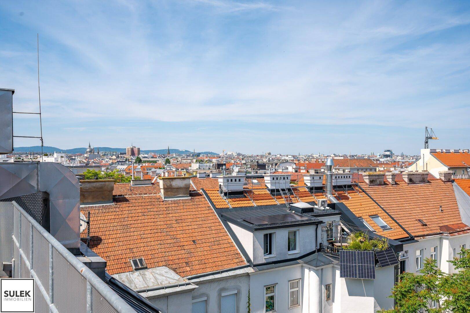 Weitläufiger Blick über die Dächer der Stadt mit vielen Gebäuden und einem klaren blauen Himmel.