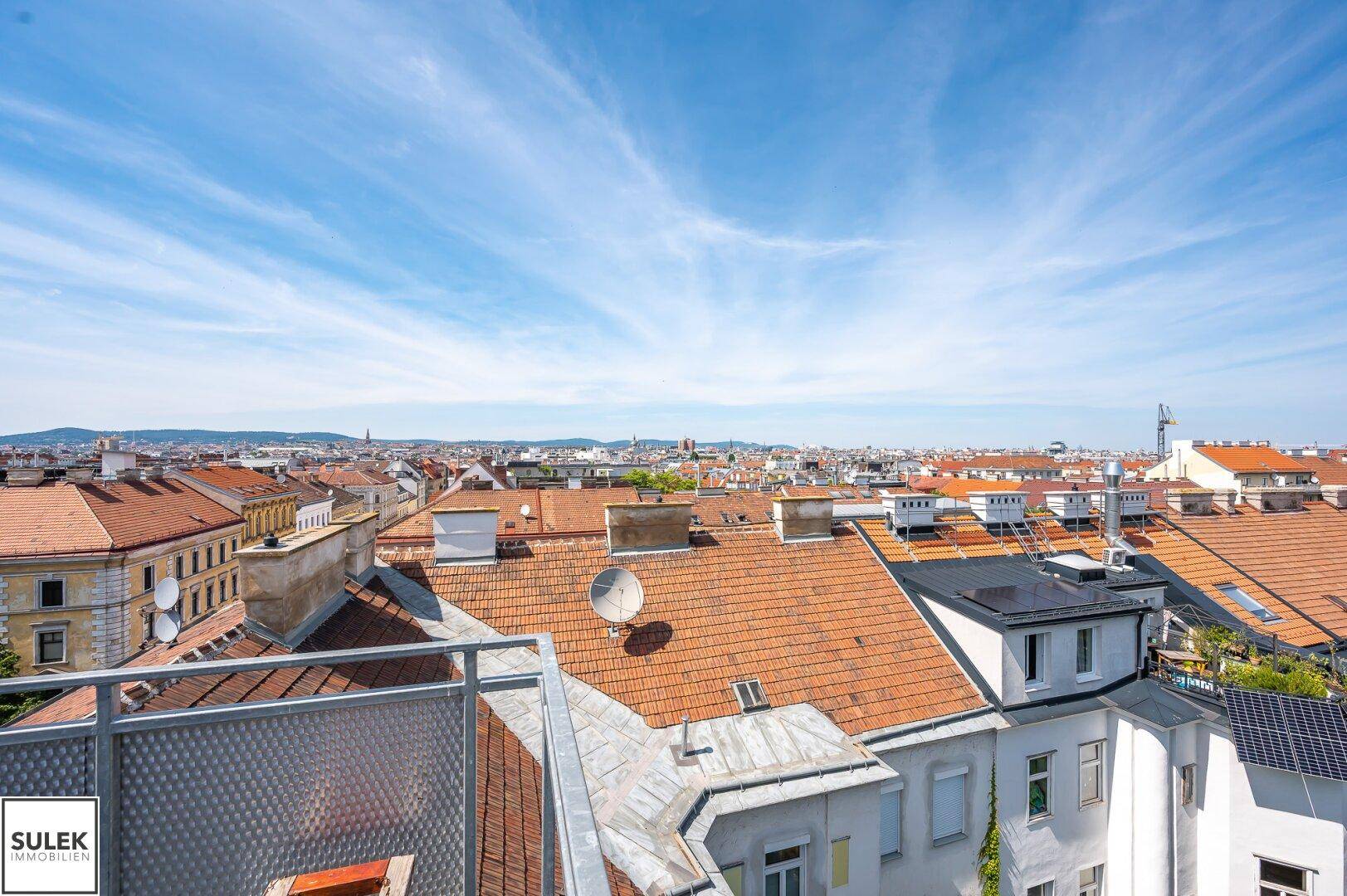 Panoramablick über die Dächer der Stadt mit Satellitenschüsseln und Solarpaneelen unter blauem Himmel.