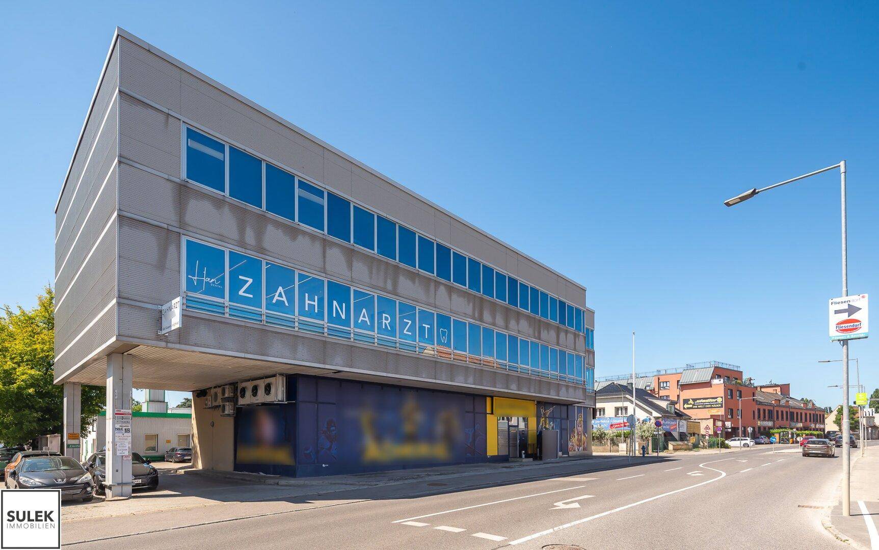Moderne Geschäftsfassade mit großen Fenstern und Zahnarztpraxis-Beschriftung an einer belebten Straße.