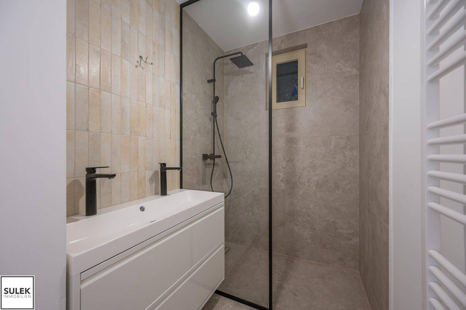 Modernes Badezimmer mit begehbarer Dusche, schwarzen Armaturen und beigefarbenen Fliesen, inklusive Fenster.