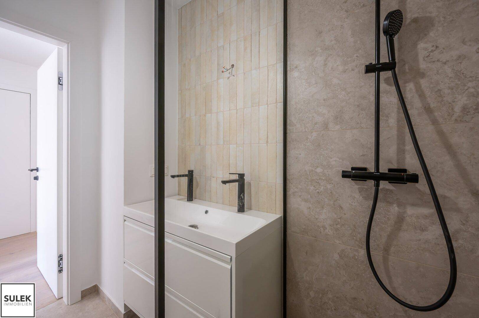 Detailansicht des modernen Badezimmers mit Waschtisch, schwarzen Armaturen und begehbarer Dusche.