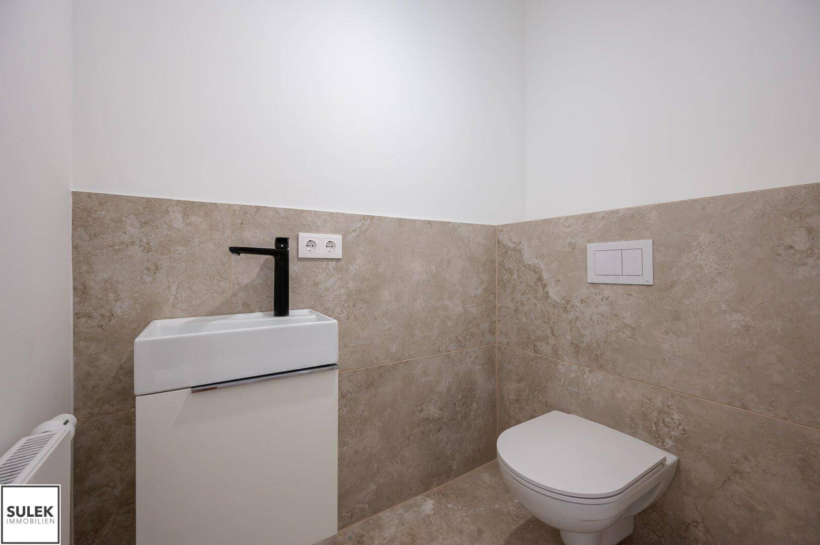 Modernes Gäste-WC mit Wand-WC, kleinem Waschtisch und beigefarbenen Fliesen an den Wänden.
