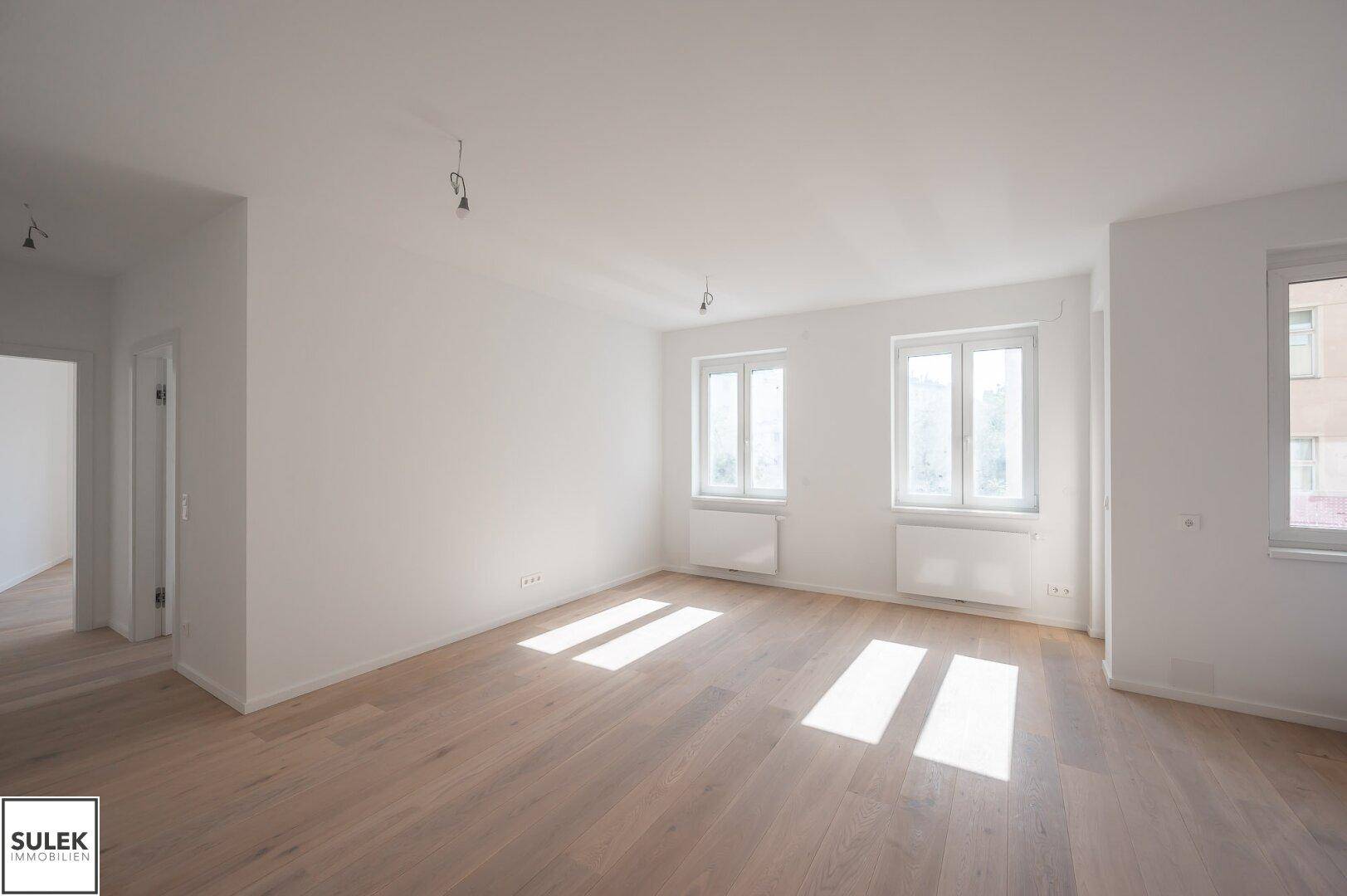 Geräumiges Zimmer mit hellem Holzboden und mehreren Fenstern, die viel Tageslicht hereinlassen.