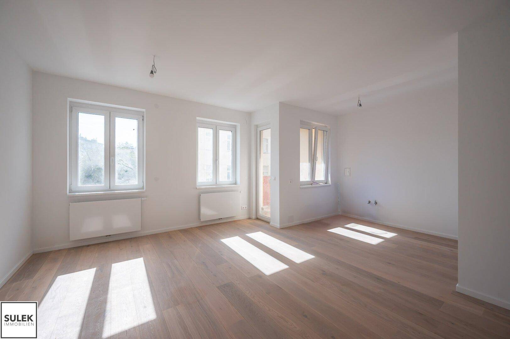 Helles und geräumiges Zimmer mit Holzboden und großen Fenstern, die den Raum mit Licht füllen.