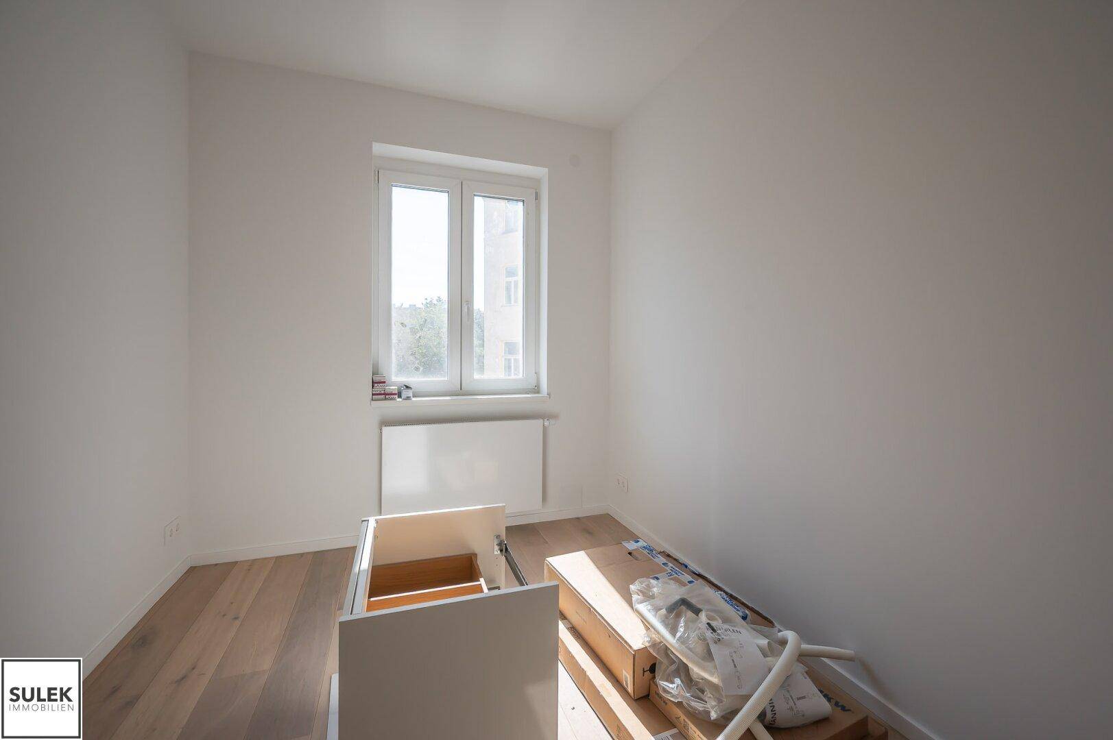 Helles Zimmer mit Holzboden und einem Fenster, bereit für die Einrichtung.